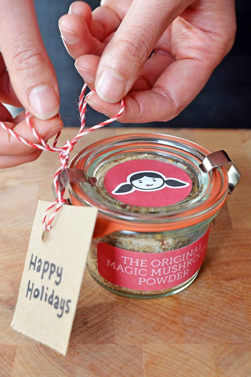 A jar of homemade Magic Mushroom Powder with a happy holidays tag.