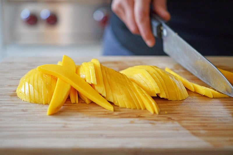 Someone slicing mango on a cutting board.