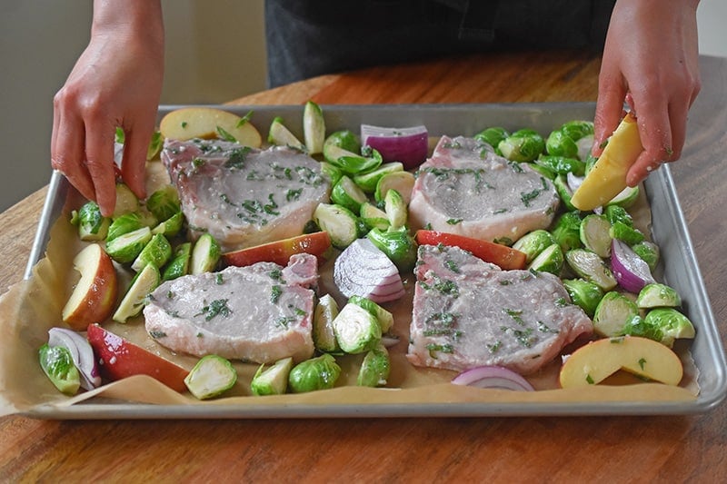 Arranging the ingredients for Sheet Pan Pork Chop Supper in a single layer on a rimmed baking sheet.