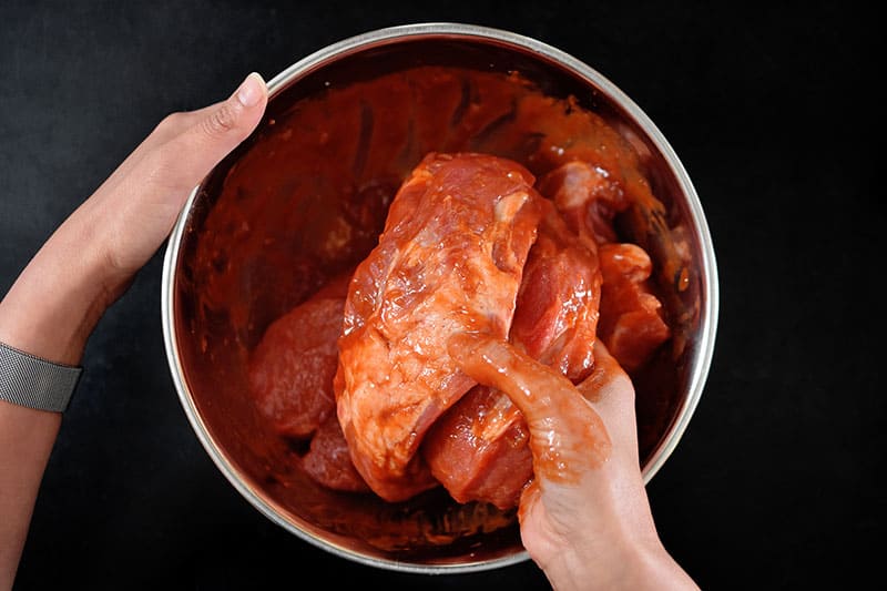 A hand is pictured mixing the Paleo Char Siu marinade with the pork shoulder pieces.