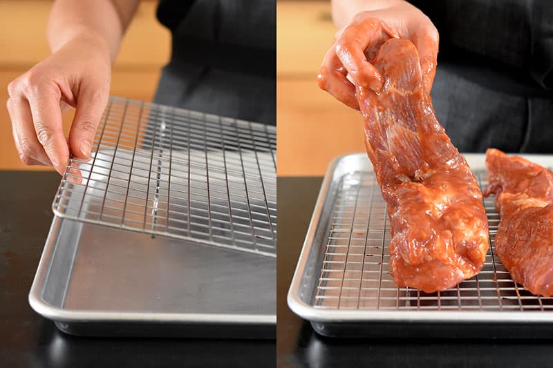 The marinated pork shoulder pieces are placed on a wire rack in a rimmed baking sheet.