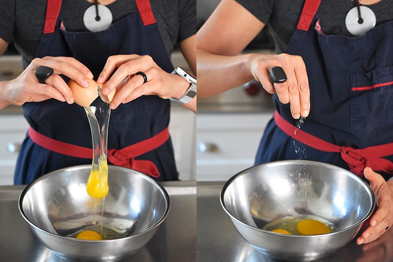 Cracking an egg into a metal bowl and sprinkling salt.