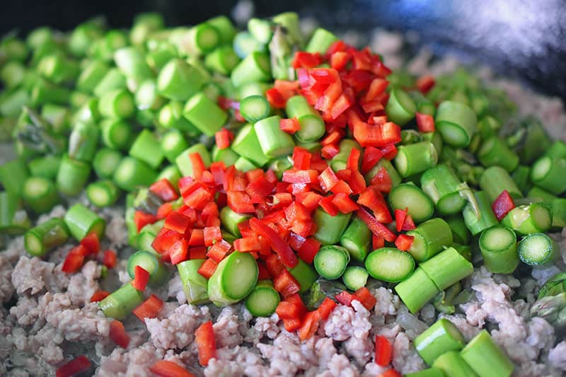 Adding minced chilis to the asparagus and ground pork in the skillet