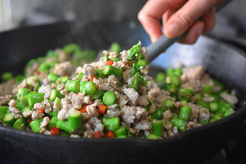 Stirring everyone in the Spicy Pork and Asparagus Stir-Fry with a gray silicone spatula to mix everything well