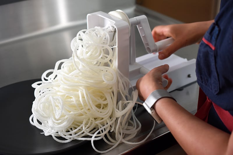 Someone using a spiralizer to spiralize daikon.