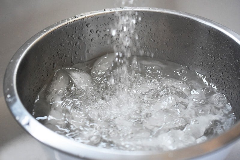 A metal bowl with ice filling with water.