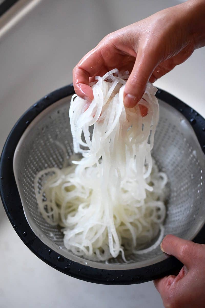 Someone pulling the chilled daikon noodles up from the colander.