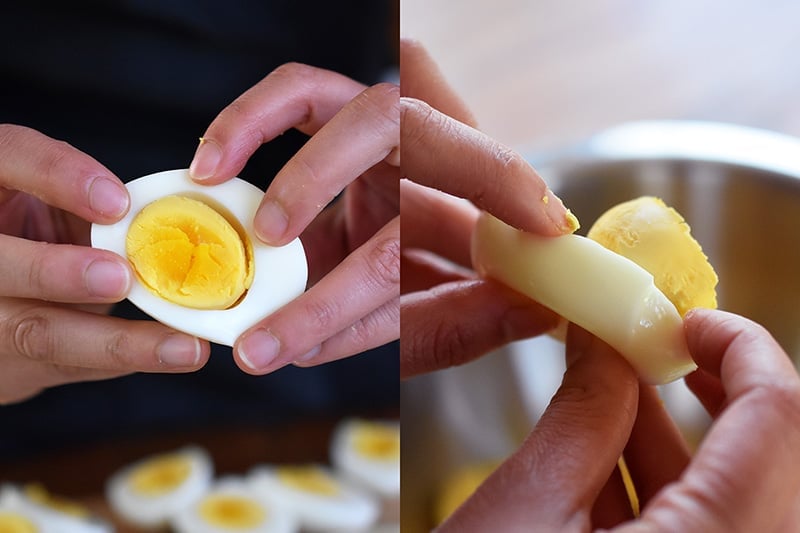 Someone popping the egg yolks out of halved hard cooked eggs.