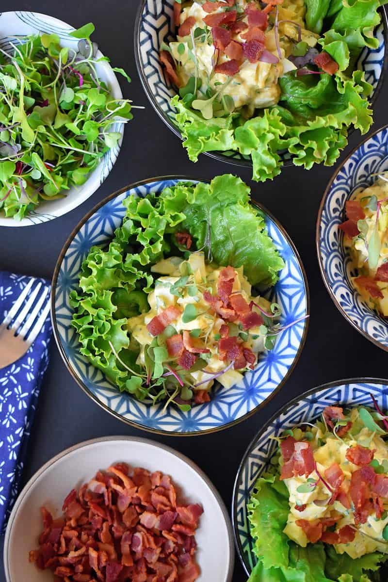An overhead shot of Bacon Deviled Egg Salad in a bunch of blue and white bowls.