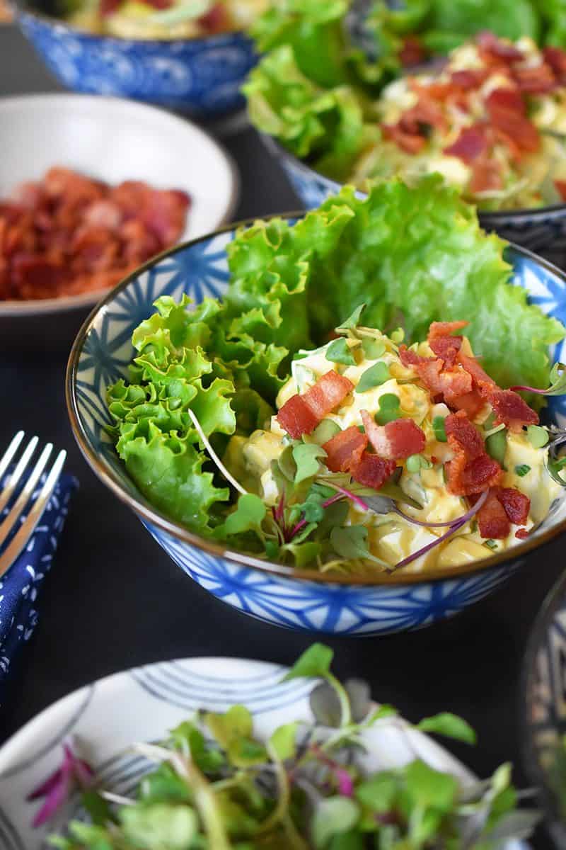 A closeup of Bacon Deviled Egg Salad on a lettuce leaf in a blue and white bowl.