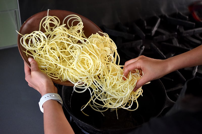 Adding spiralized sweet potatoes to a cast iron skillet.
