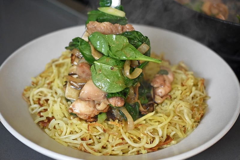 Tranferring the Paleo Chicken Chow Mein topping on top of a white plate filled with crispy spiralized sweet potato noodles.