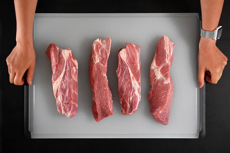 Four pieces of pork shoulder on a cutting board.