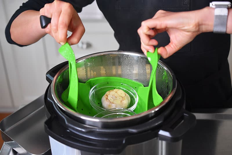 Someone lifting out roasted garlic out of the instant pot.