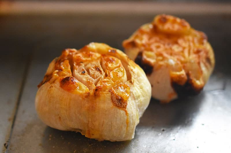 Two bulbs of roasted garlic sitting on a sheet pan.