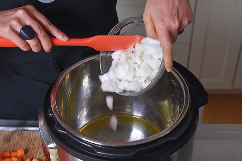 Someone adding chopped onions to an Instant Pot with oil.