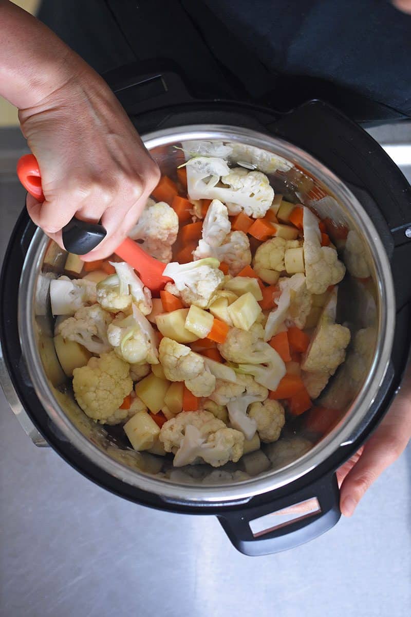 Someone stirring parsnips, carrots, and cauliflower in an Instant Pot with a rubber spatula.