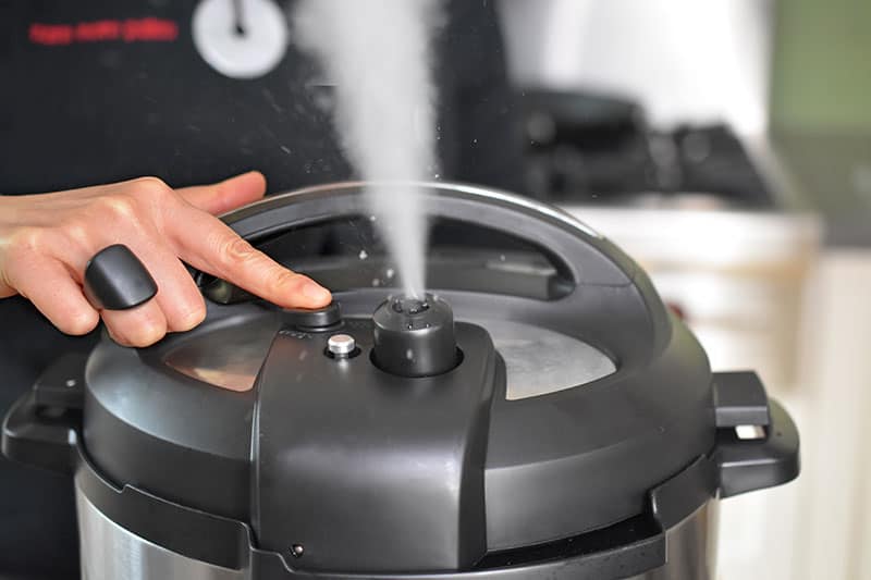 Someone pressing the button to manually release the pressure in an Instant Pot.