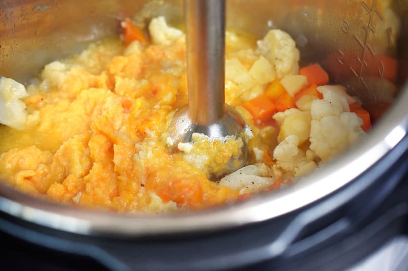 Someone pureeing the autumn mash mixture with an immersion blender inside an Instant Pot.