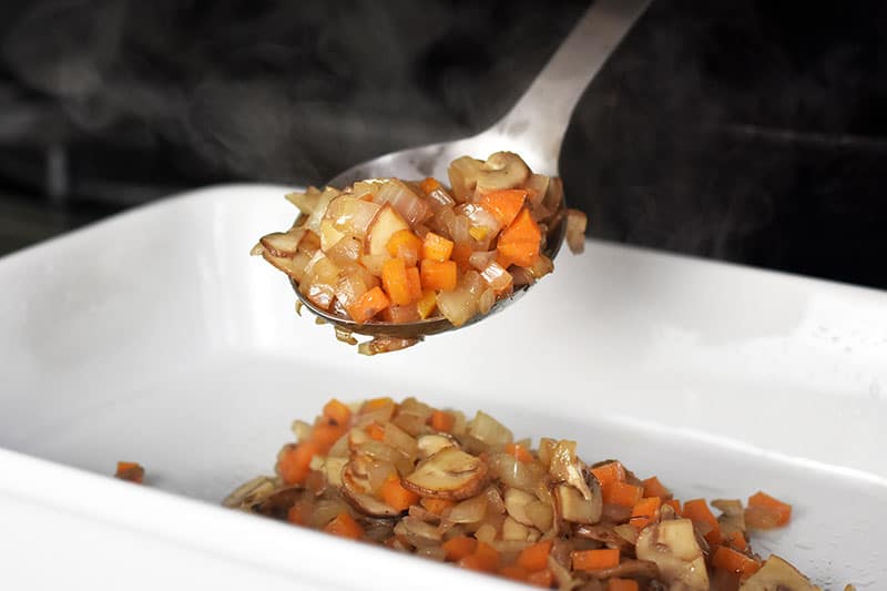 The vegetable filling for Italian Sausage + Kale Casserole is spooned into a greased casserole dish.