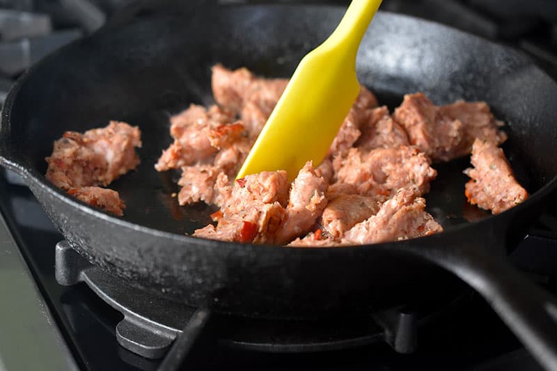 Bulk Italian Sausage is cooked in a large cast iron skillet.