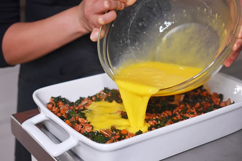 A bowl of whisked eggs is poured into the casserole dish.