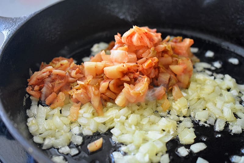 Kimchi on fried onions in a pan.