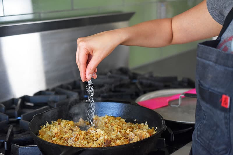 Someone sprinkling salt into a pan with fried cauliflower kimchi fried rice.