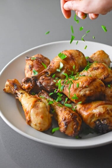 Someone sprinkling minced Italian parsley on a bowl of paleo Orange Dijon Chicken, a Whole30 and low carb simple chicken dinner.