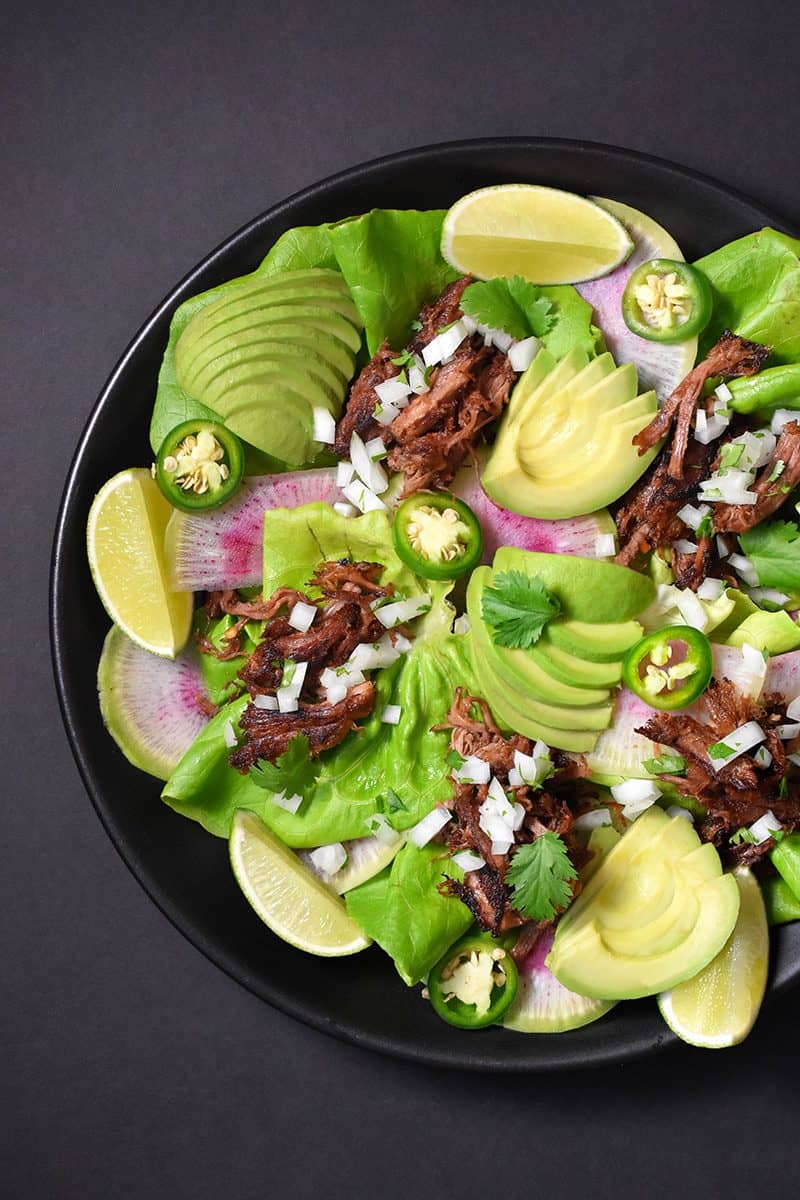 Instant Pot carnitas in a bowl with lettuce, limes, avocados, and jalapenos.