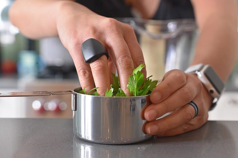 Someone packing a measuring cup with arugula for arugula pesto.