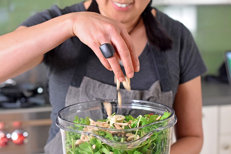 Someone adding slivered almonds to a food processor with arugula.