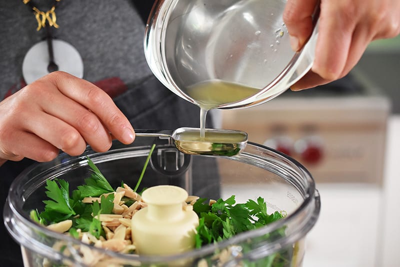 Someone pouring lemon juice into a measuring spoon on top of a food processor.