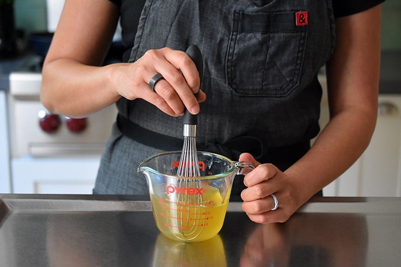 Someone whisking together the vinegar, juice, and salt in a measuring cup to make paleo, Whole30, and vegan quick pickled red onions.