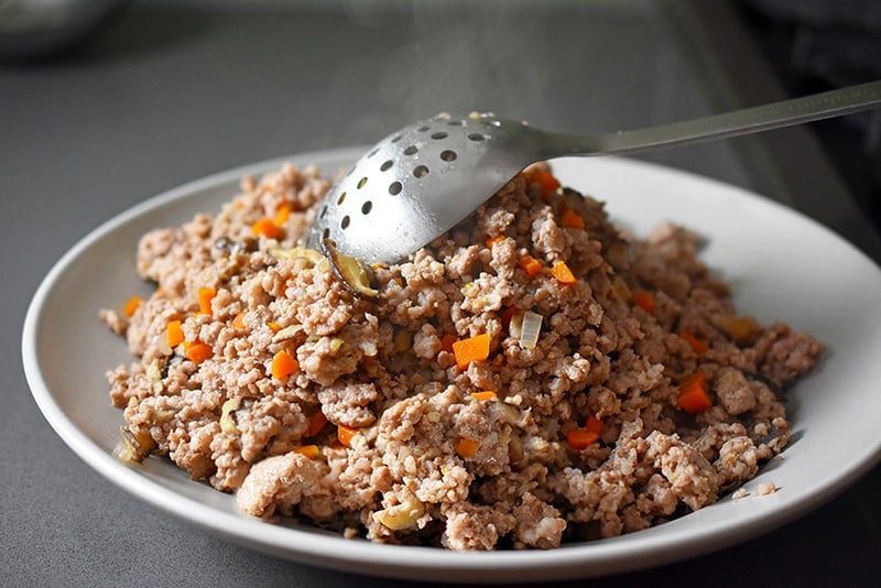 Using a slotted spoon to transfer the pork and vegetables to another plate 