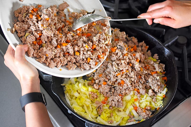 Adding the cooked pork back into the skillet with the napa cabbage.