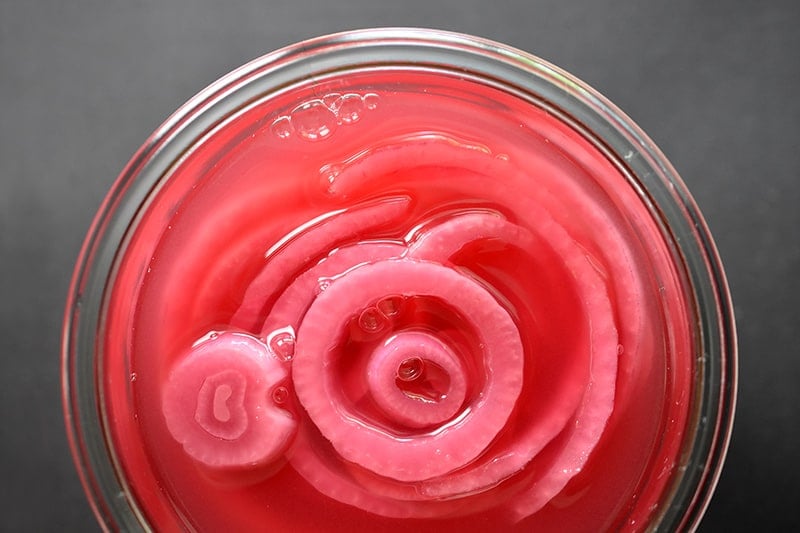 An overhead shot of an open glass jar filled with quick pickled red onions.