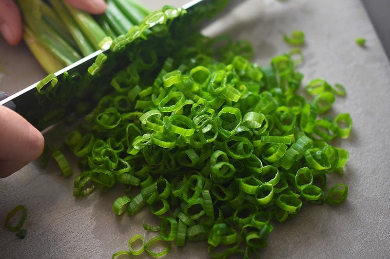 A closeup shot of someone thinly slicing scallions to make Paleo and gluten-free Scallion Pancakes 