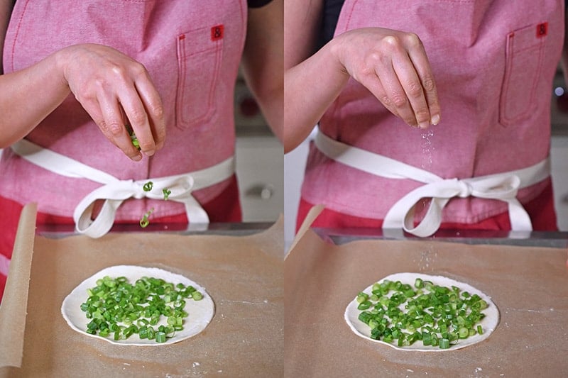 Sprinkling scallions and salt on a flattened piece of cassava flour dough to make Paleo Scallion Pancakes 
