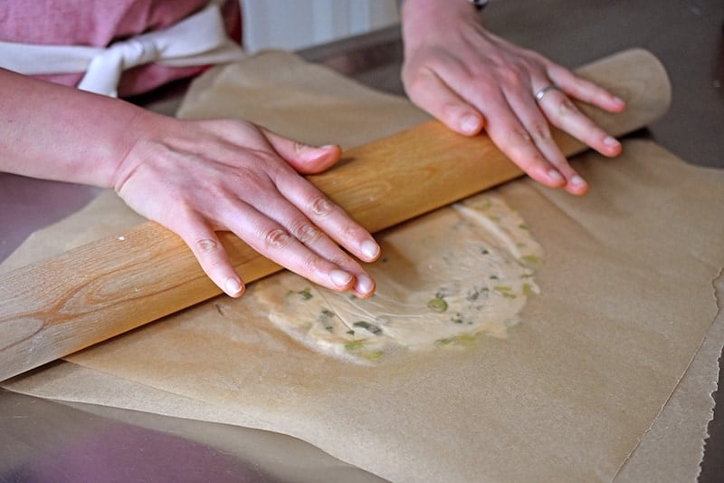 A shot of someone rolling out the Paleo Scallion pancake dough between parchment paper with a rolling pin.