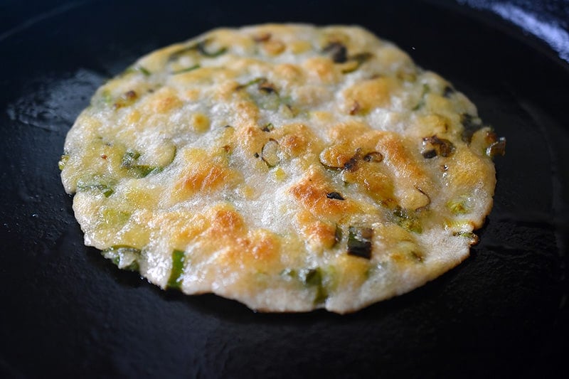 A closeup shot of a crispy Paleo Scallion Pancake in a cast iron skillet.