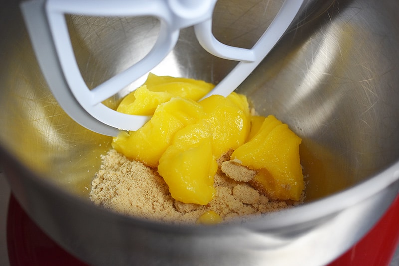 A stand mixer bowl has ghee and maple sugar in it, along with the paddle attachment.