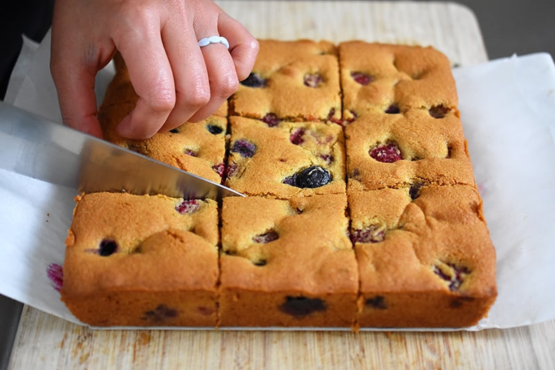 Someone cutting a paleo and gluten-free berry snack cake into nine evenly sized pieces.