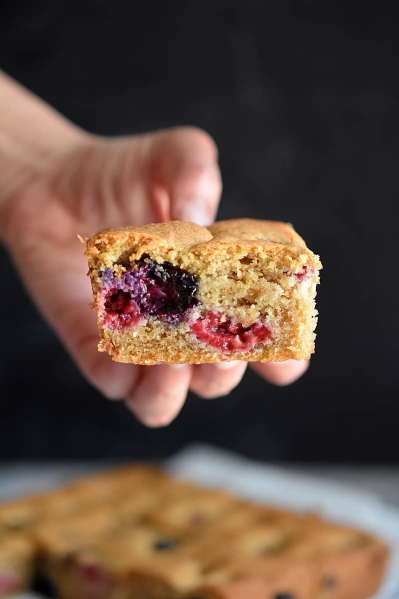 Someone holding a square slice of paleo and gluten-free berry snack cake.