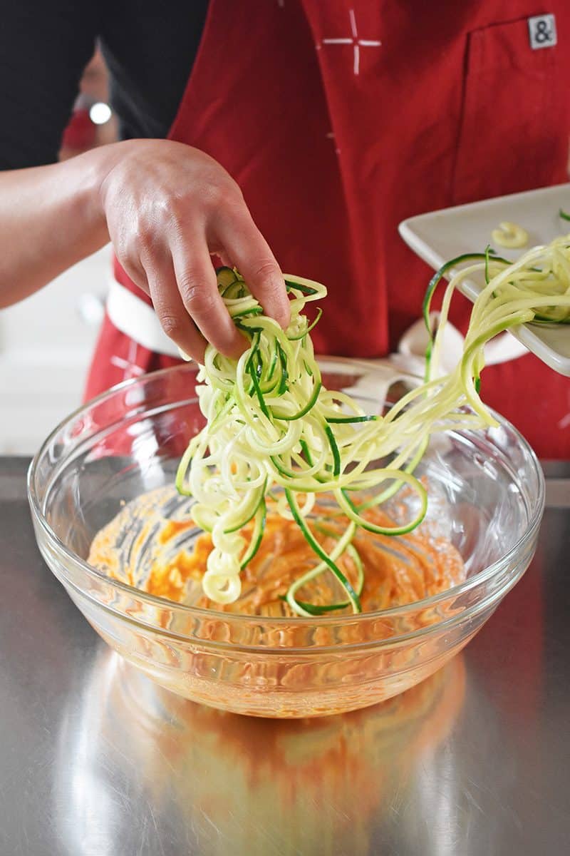 Someone adding raw zoodles in a bowl with the spicy Thai marinade.