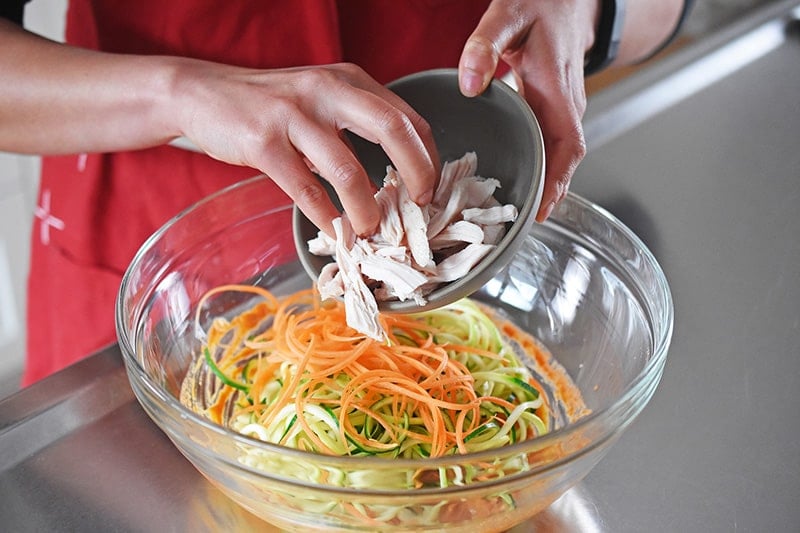 Someone adding cooked chicken to a bowl with julienned vegetables.