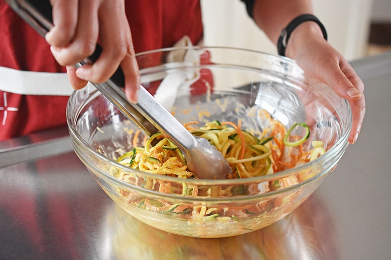 Someone mixing julienned vegetables with the spicy Thai marinade.
