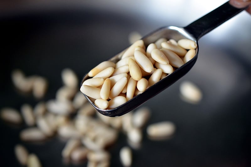 Pine nuts measured in a measuring spoon being put into a pan to be toasted.