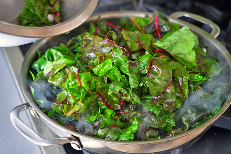 Adding the swiss chard leaves to a large hot pan for a swiss chard salad.