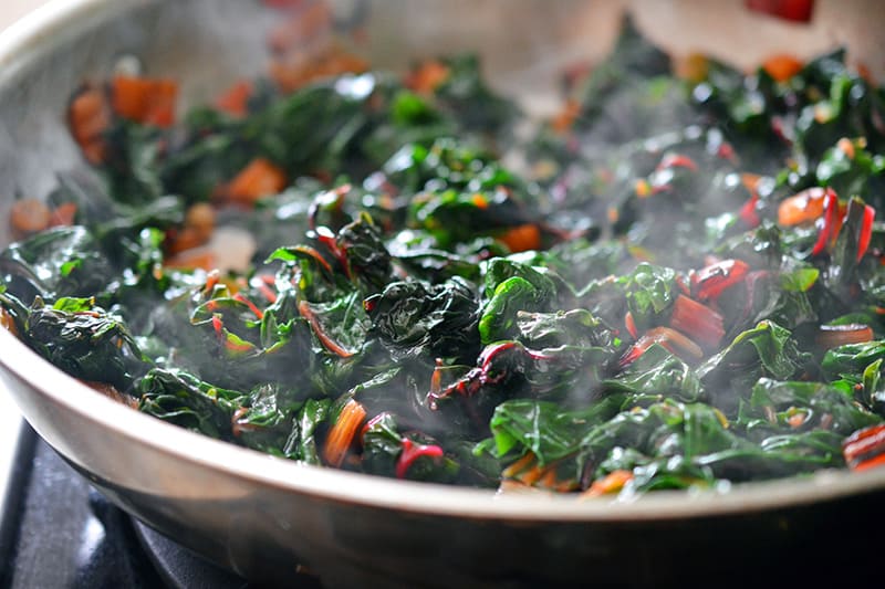 Sautéeing swiss chard in a pan for a swiss chard salad.